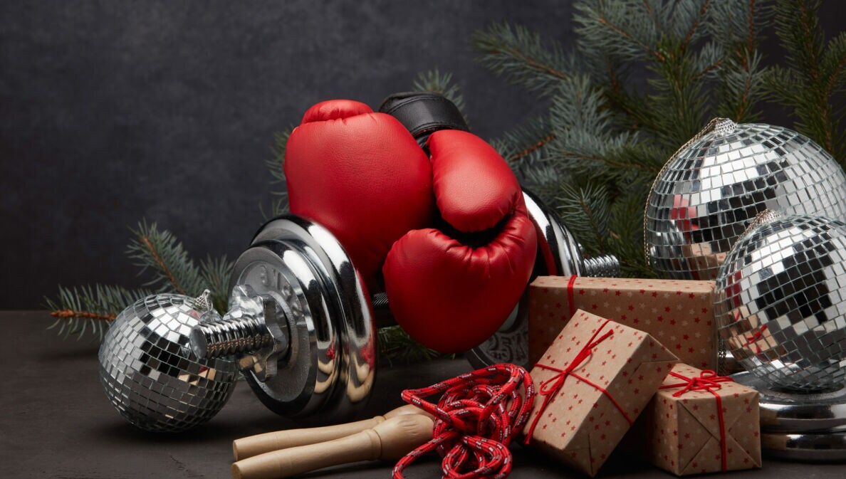 Stillleben mit roten Sportutensilien und Geschenken mit Tannenzweig vor dunklem Hintergrund