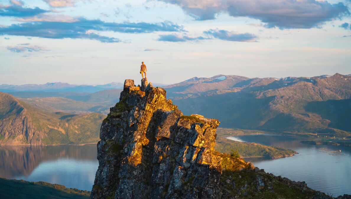 Eine Wanderin auf einem Felsen an einem Fjord.