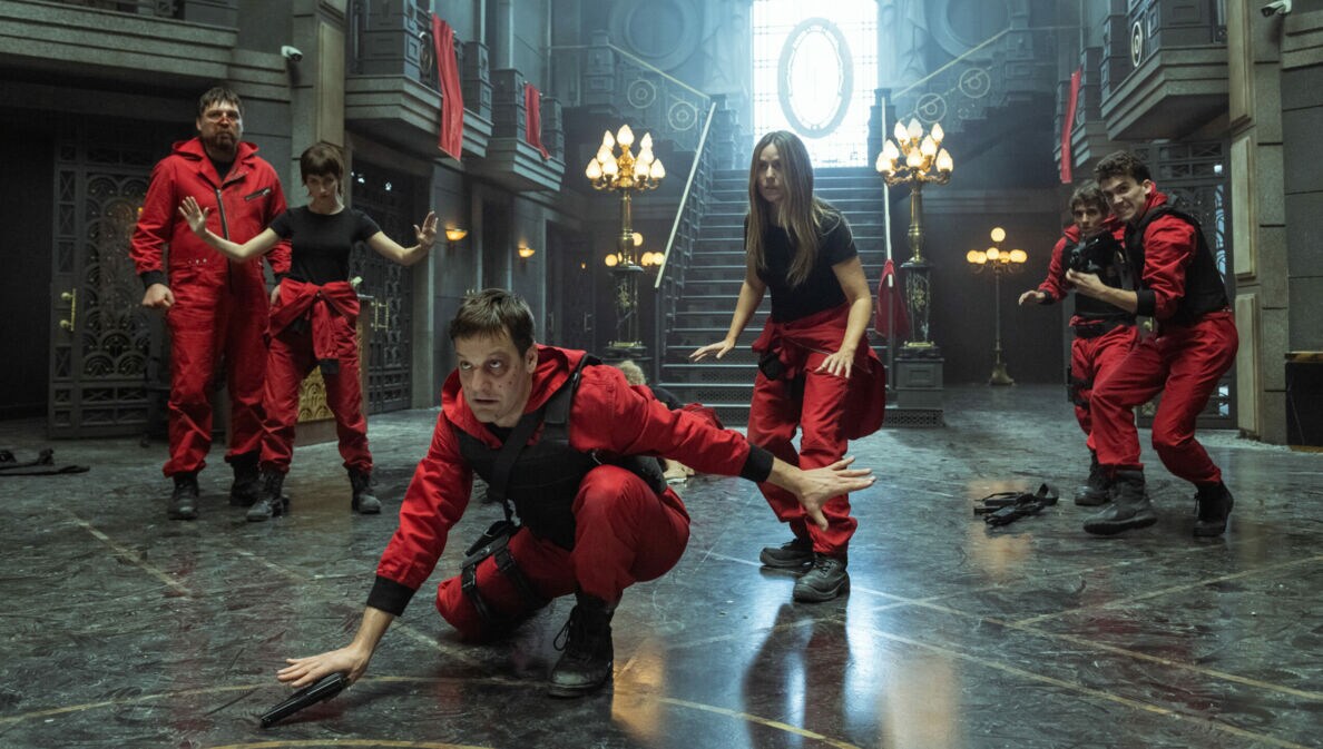 Fünf Personen in roten Anzügen in defensiver Haltung in einer prächtigen Eingangshalle aus Stein und Marmor