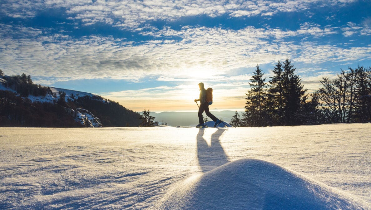 Eine Frau läuft auf einer Loipe mit Blick in die Berglandschaft in der Wintersonne