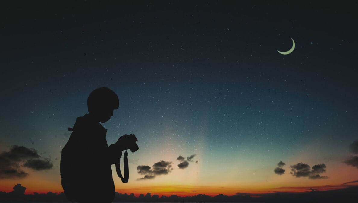 Ein Fotograf sieht in der Dunkelheit auf seine Kamera, am Himmel steht der Mond.