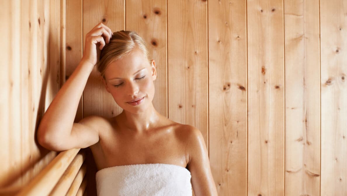 Eine junge Frau entspannt im weißen Handtuch in einer Sauna