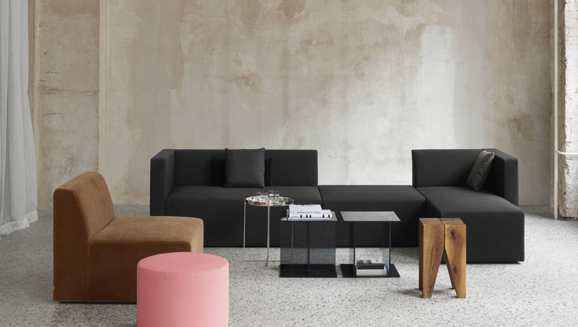 Sitzgruppe aus minimalistischen Polstermöbeln und Beistelltischen in einem hellen Raum mit Betonwand
