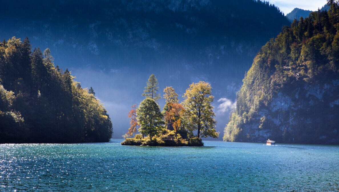 Ein großer See mit einer Insel mit herbstlichen Laubbäumen, eingebettet von riesigen Felswänden
