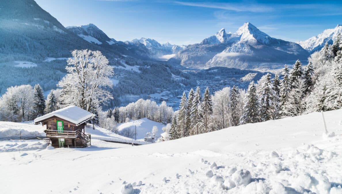 Eine schneebedeckte Berglandschaft, im Vordergrund steht eine kleine Holzhütte