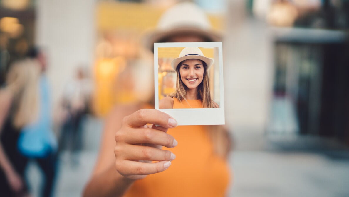Eine junge Frau hält ein Polaroid in der Hand mit einem Selbstportrait