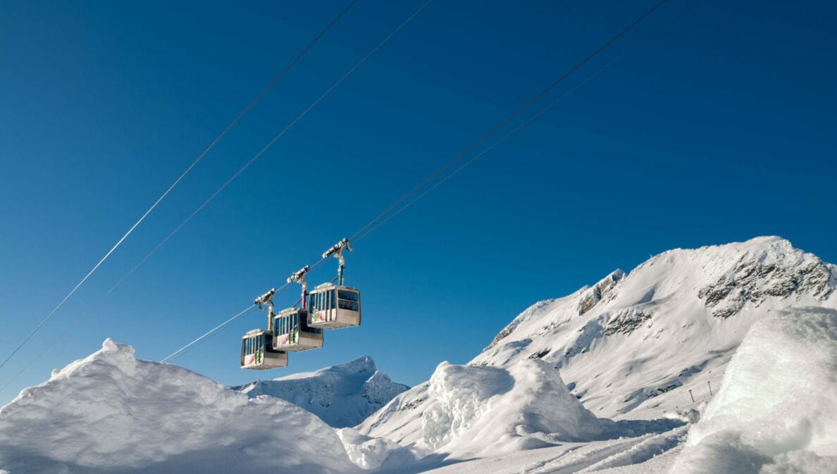 Eine Seilbahn vor blauem Himmel und schneebedeckten Bergen