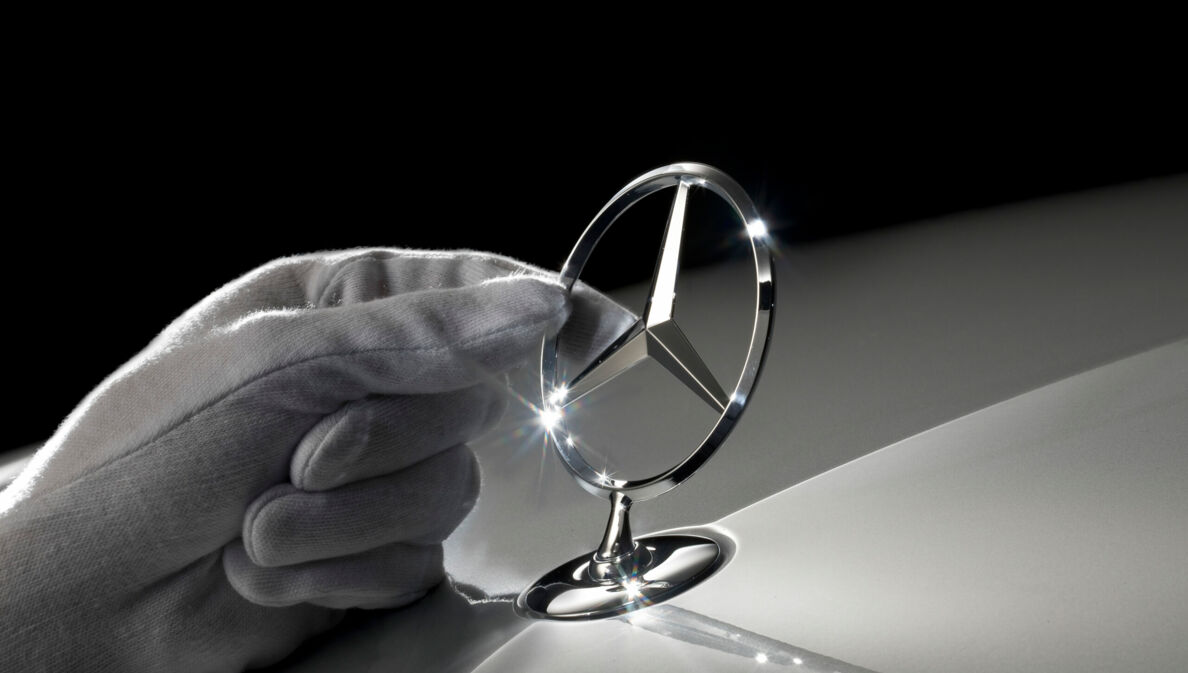 Eine Hand fasst einen Mercedes-Stern an.