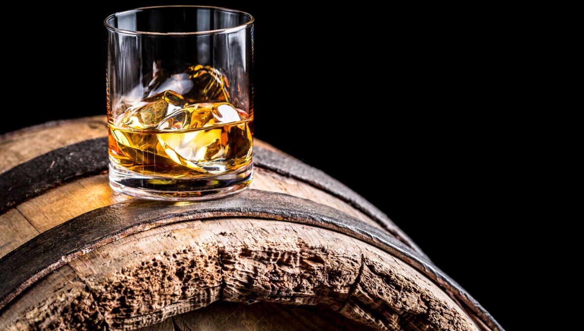 Ein Glas Whiskey mit Eiswürfeln auf einem alten hölzernen Barrel