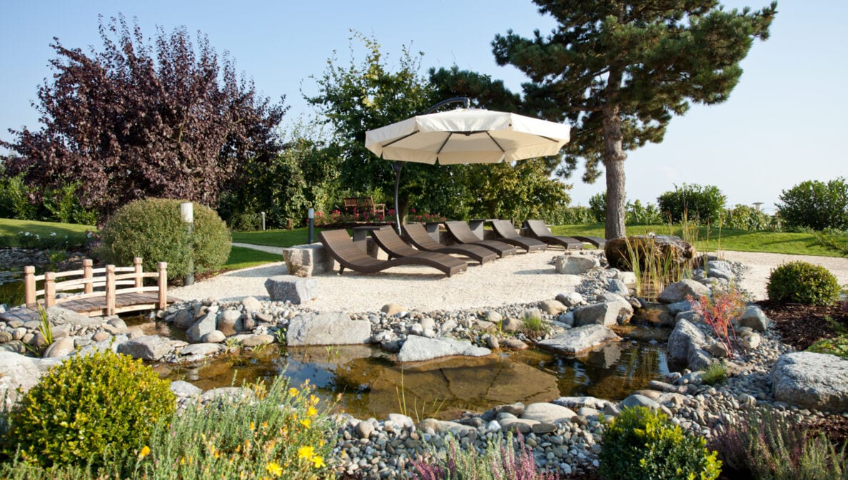 Ein gestalteter Garten mit Liegestühlen an einem bepflanzten Teich