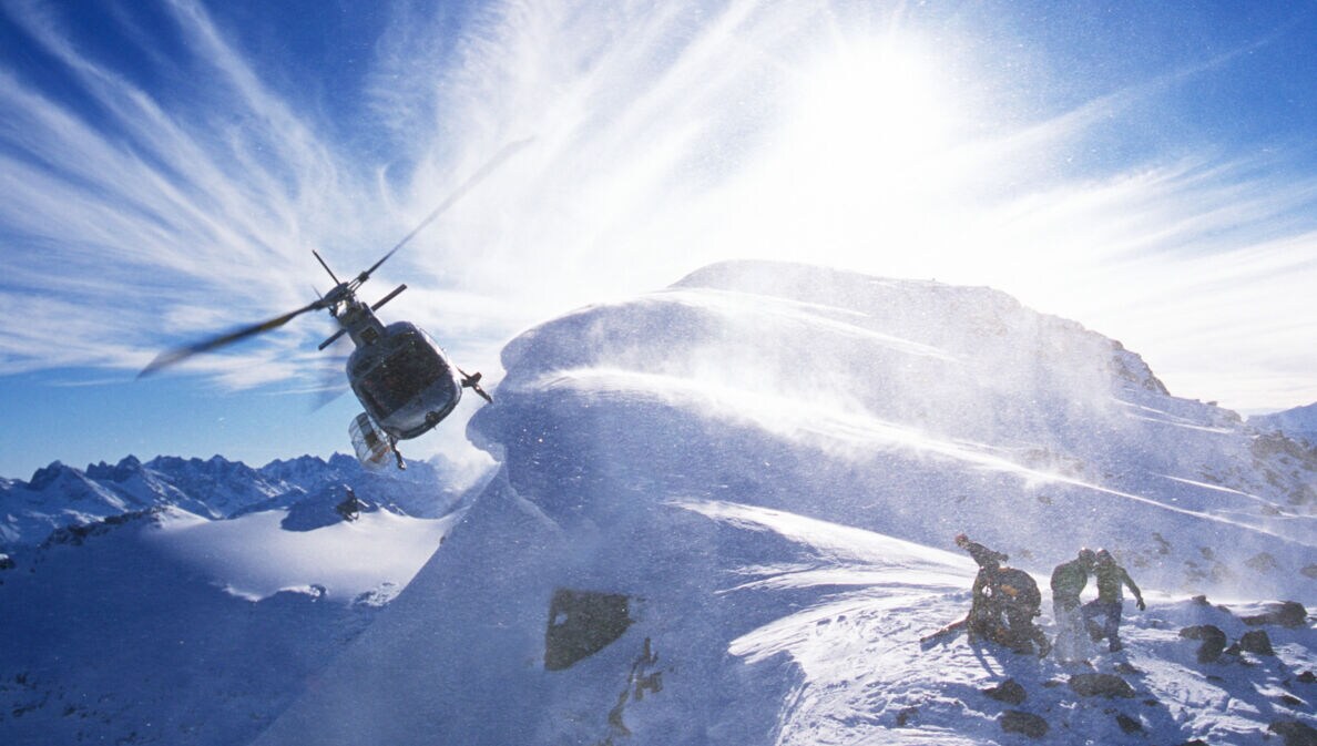 Ein Hubschrauber an einem verschneiten Berggipfel mit einer Personengruppe mit Snowboards
