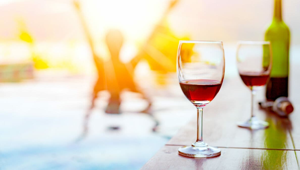 Zwei Gläser Rotwein stehen am Rand eines Schwimmbeckens.