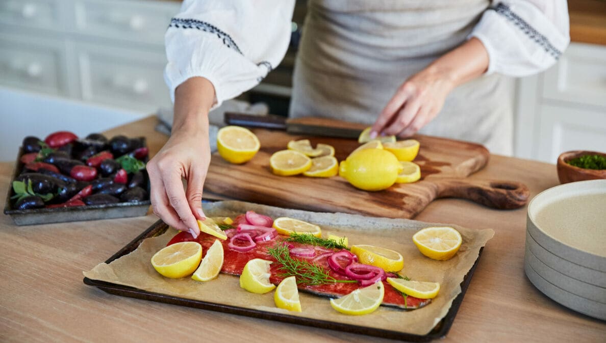 Eine Frau bereitet Lachs mit Zitronenscheiben auf einem Blech in einer Küche zu