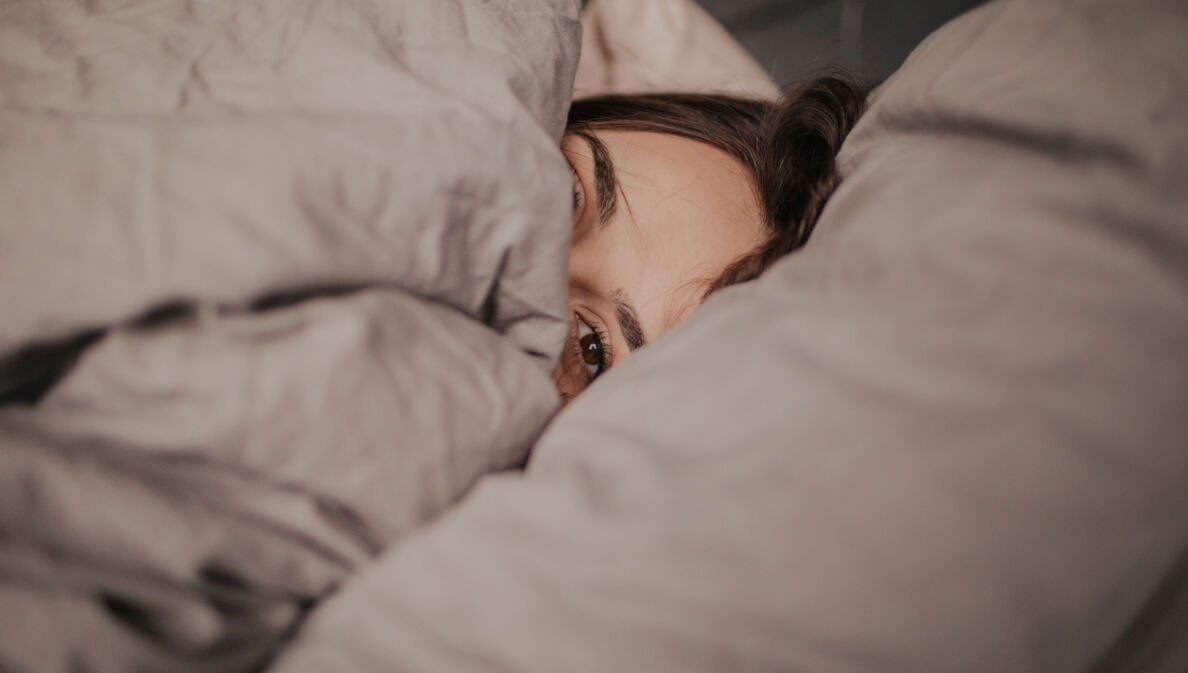 Eine Frau liegt unter einer Bettdecke im Bett