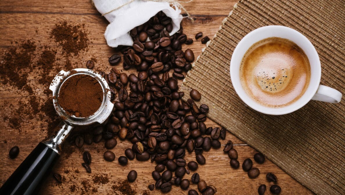 Kaffeebohnen, Espresso mit Crema und Espressopulver liegen auf einem Brett