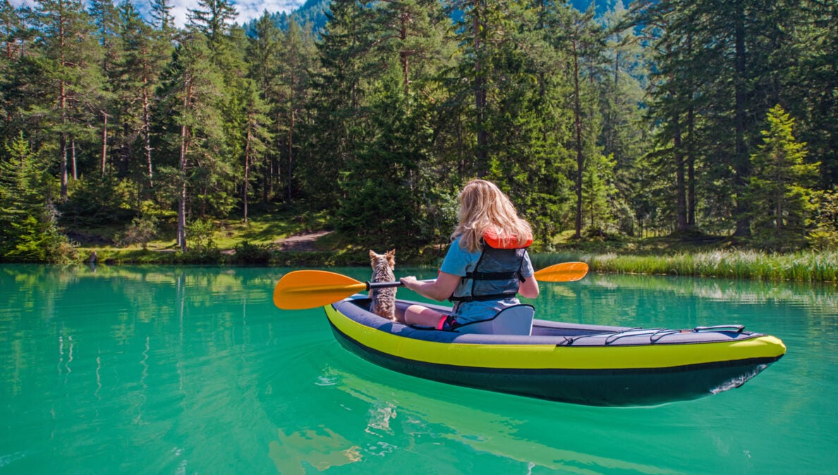 Eine Frau mit einem Hund im Kanu auf einem türkisfarbenen Fluss