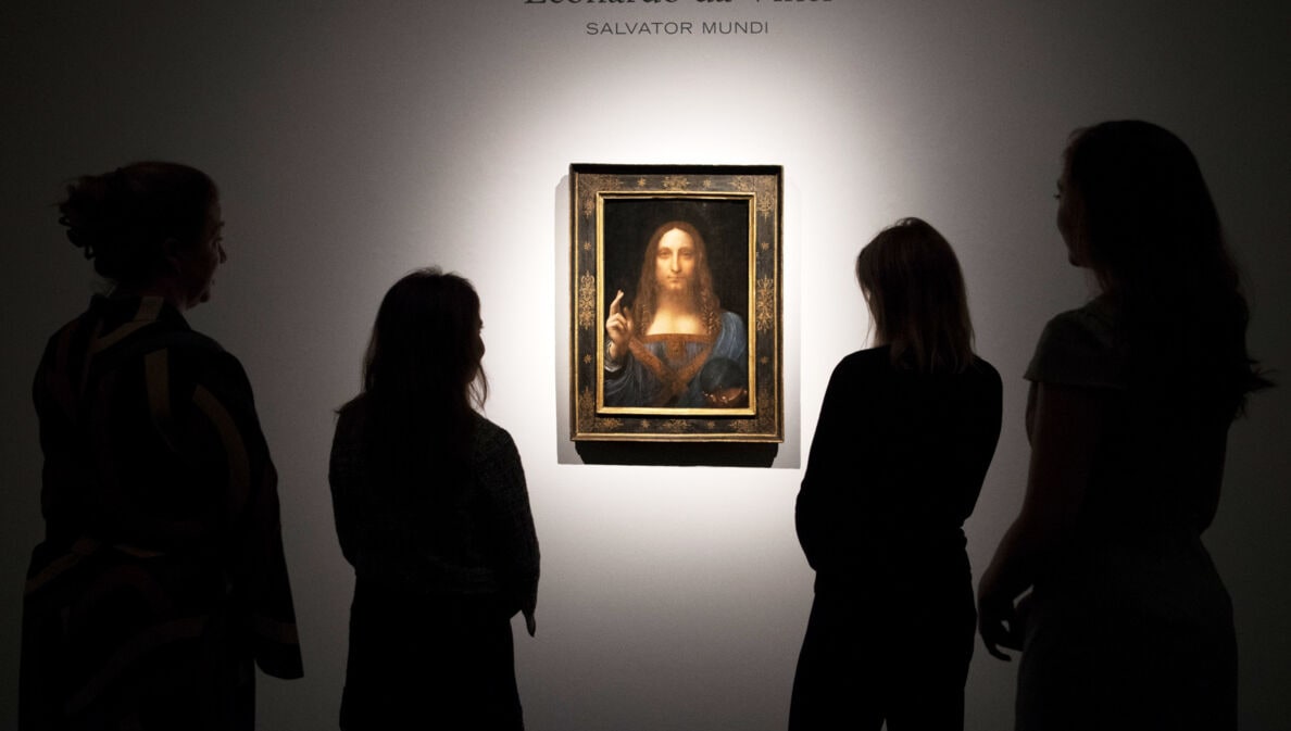 Rückansicht mehrerer Personen als Silhouetten, die Leonardo da Vincis Gemälde Salvator Mundi in einem goldenen Rahmen an einer weißen Wand betrachten