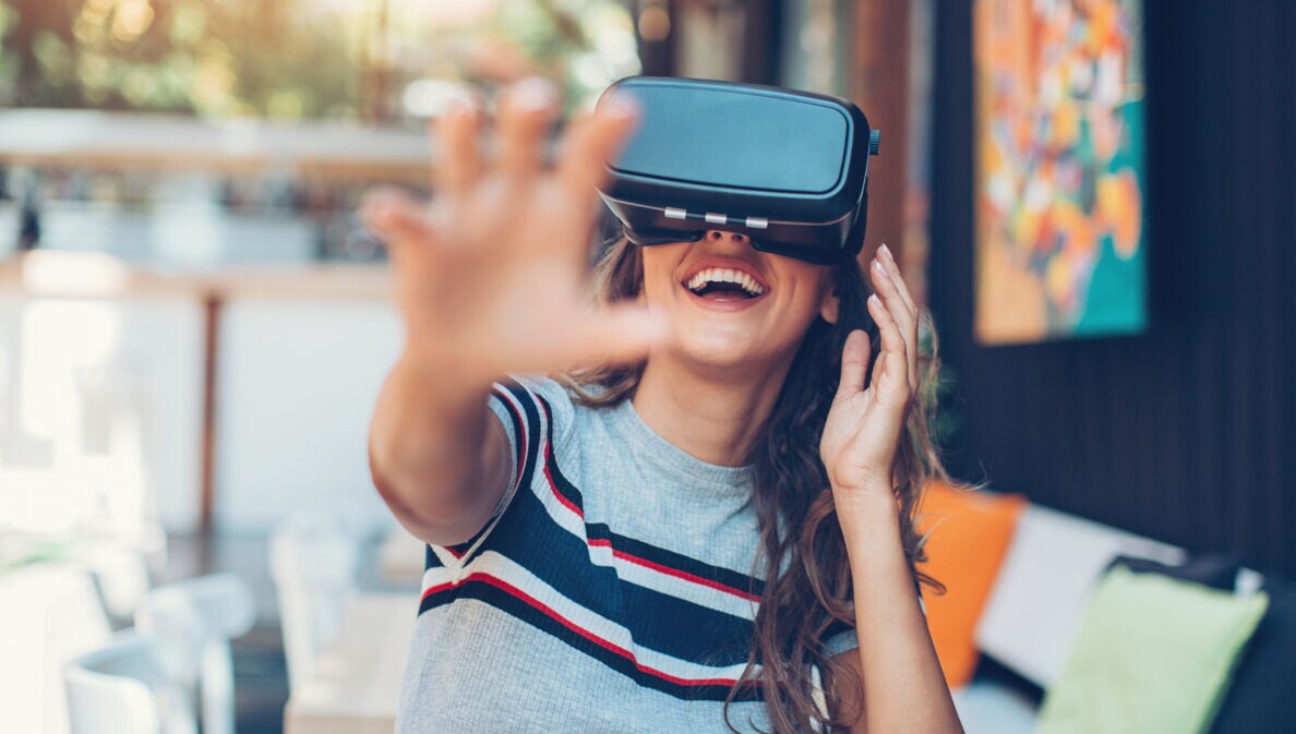 Eine Frau mit VR-Brille lacht und greift in die Luft