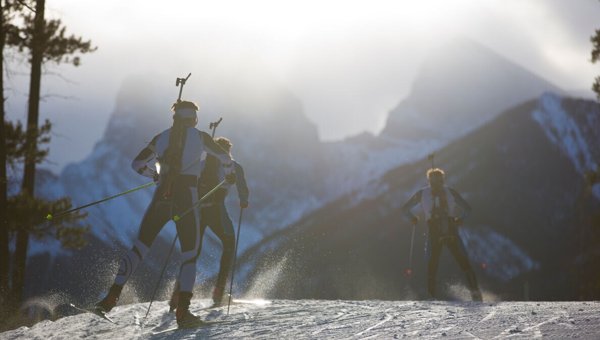 Drei Männer auf Skiern mit einem Biathlon-Gewehr auf dem Rücken fahren durch den Schnee.
