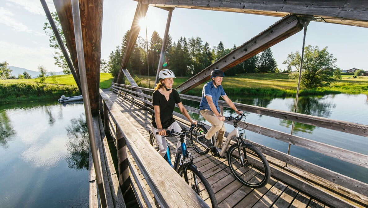 Ein Paar auf Fahrrädern fährt über eine Holzbrücke über einen Fluss