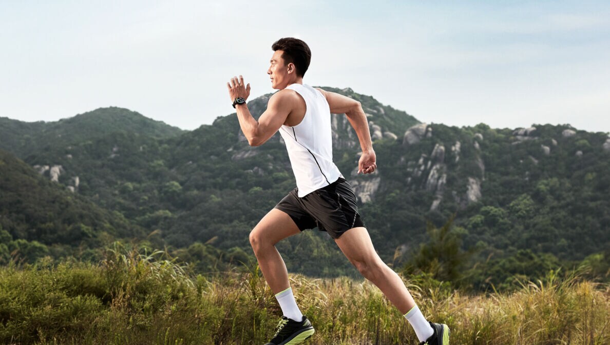 Mann joggt im Sportdress, im Hintergrund ein bewaldeter Berg