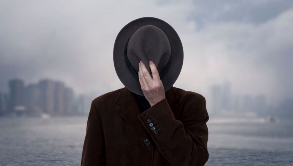 Ein Schwarz-Weiß-Bild einer Person, die sich einen Hut vor das Gesicht hält