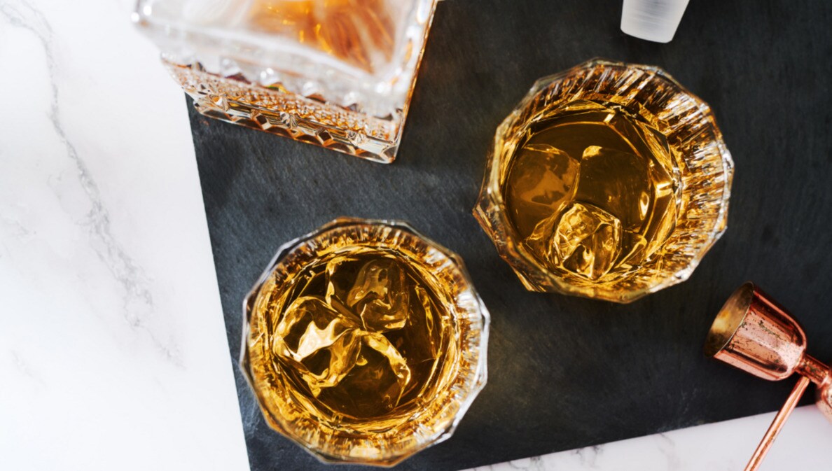 Aufsicht von zwei gefüllten Whiskygläsern mit Eis auf einer Schieferplatte