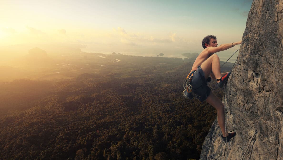 Ein junger Mann klettert an einer Felswand, während die Sonne untergeht