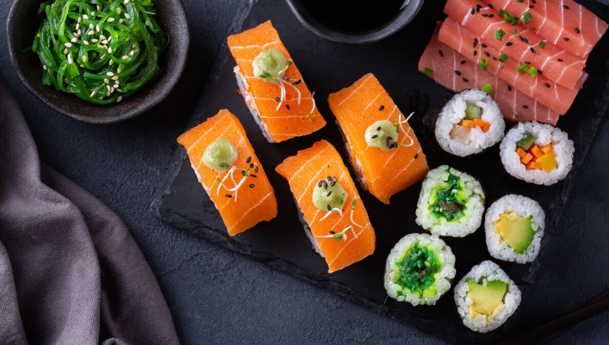 Veganes Sushi auf einer Schieferplatte angerichtet mit Sojasoße und Algensalat