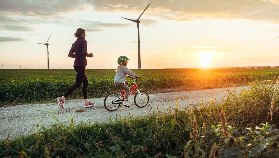 Eine joggende Frau ist mit einem kleinen Mädchen auf dem Fahrrad bei Sonnenuntergang unterwegs