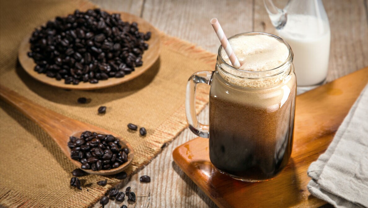 Ein Glas Nitro-Coffee auf einem Tisch mit Kaffeebohnen