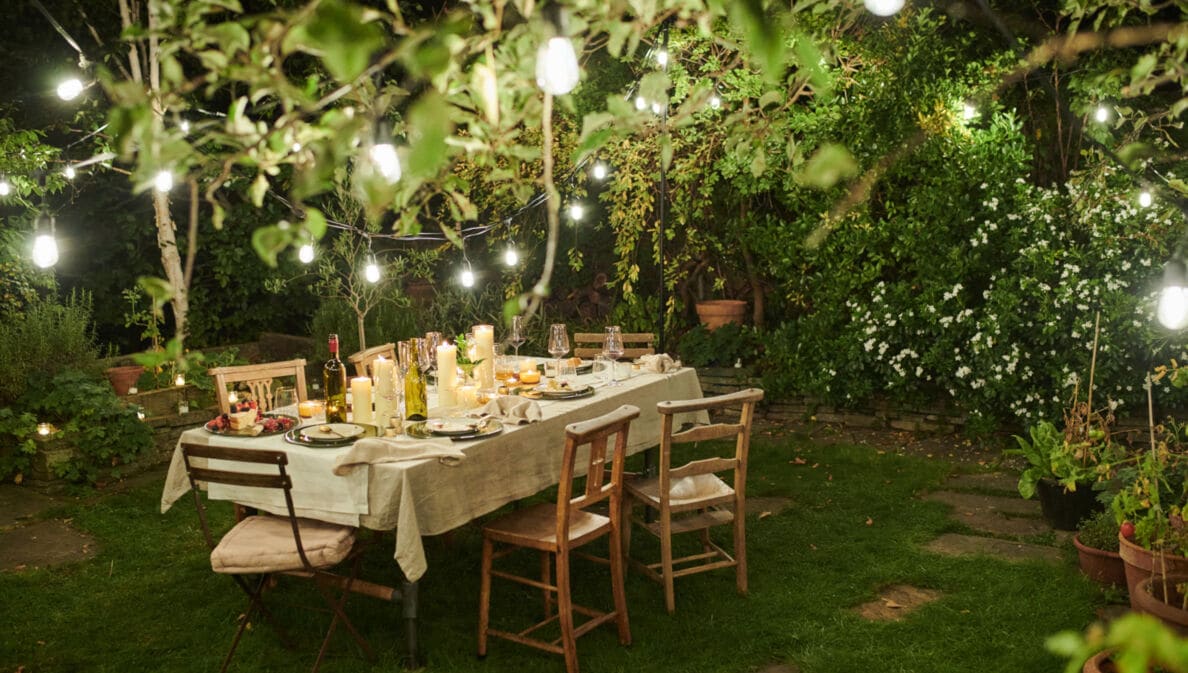 Ein gedeckter Tisch in einem Garten mit stimmungsvoller Beleuchtung bei Nacht