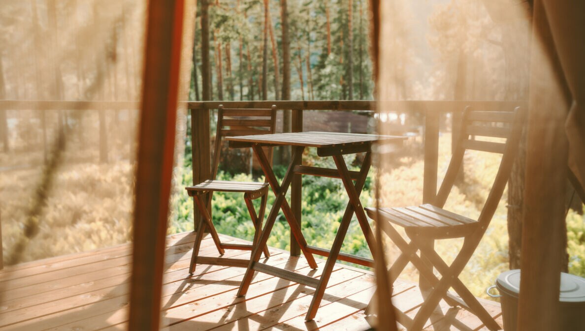 Blick auf eine Holzterrasse mit Stühlen und Tisch, im Hintergrund Wald