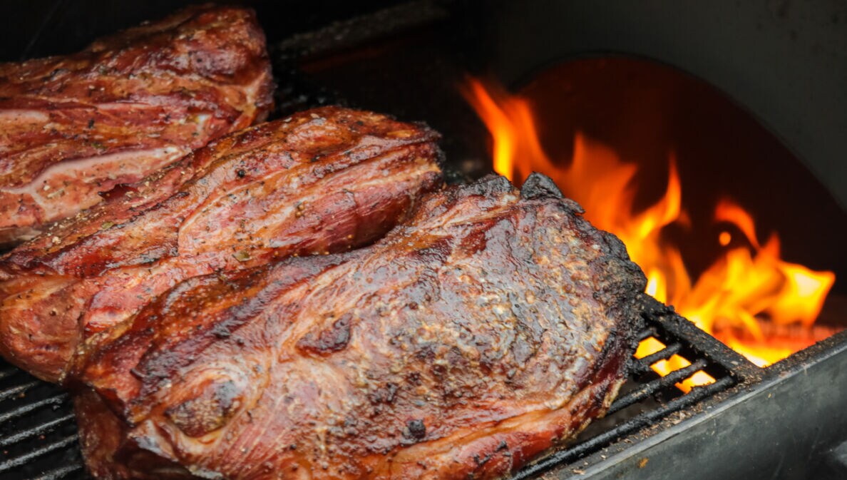 Fleisch wird indirekt neben einer Flamme im Grill gegrillt