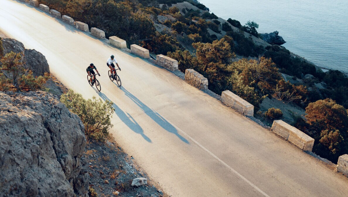 Zwei professionelle Radfahrer fahren mit ihren Rennrädern eine Küstenstraße entlang