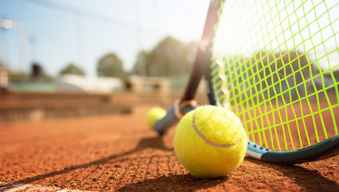Tennisball und Schläger auf einem Tennisplatz bei schönem Wetter