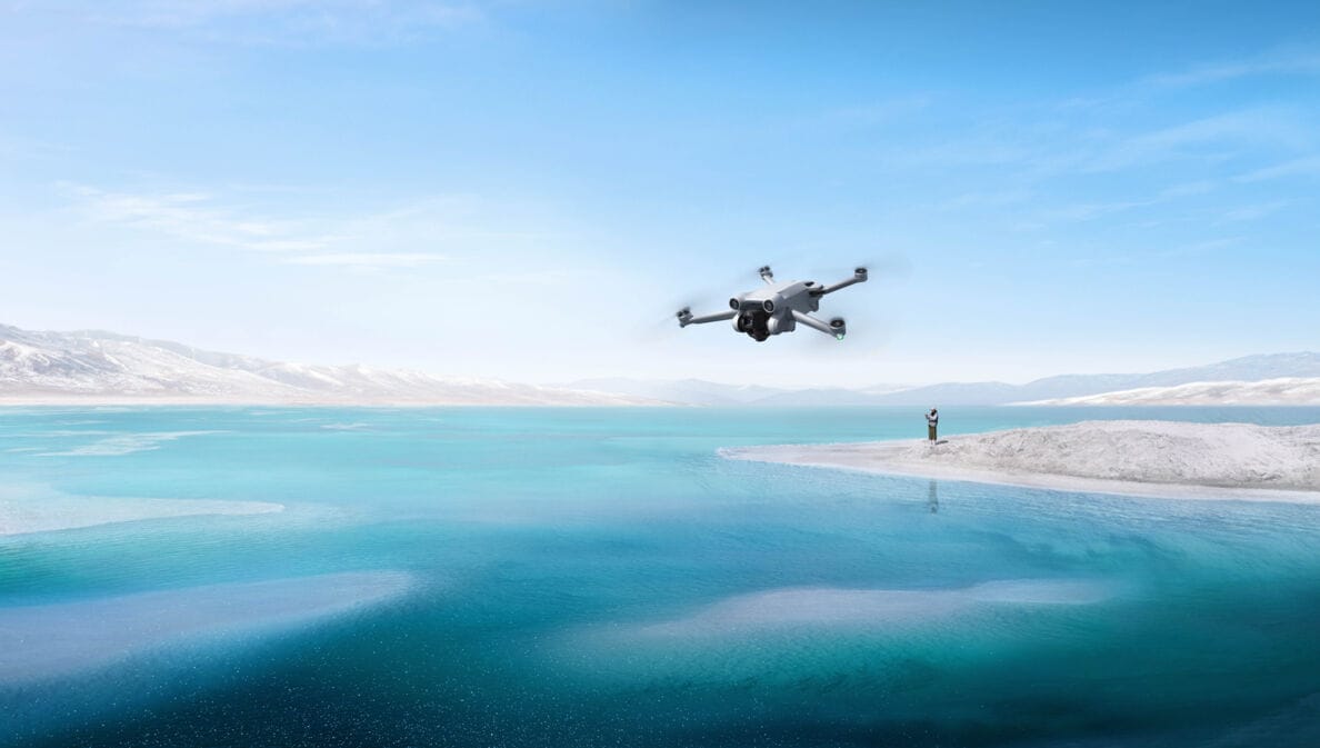 Drohne DJI Mini 3 Pro wird von einer Person in weiter Entfernung über einen kristallblauen See geflogen