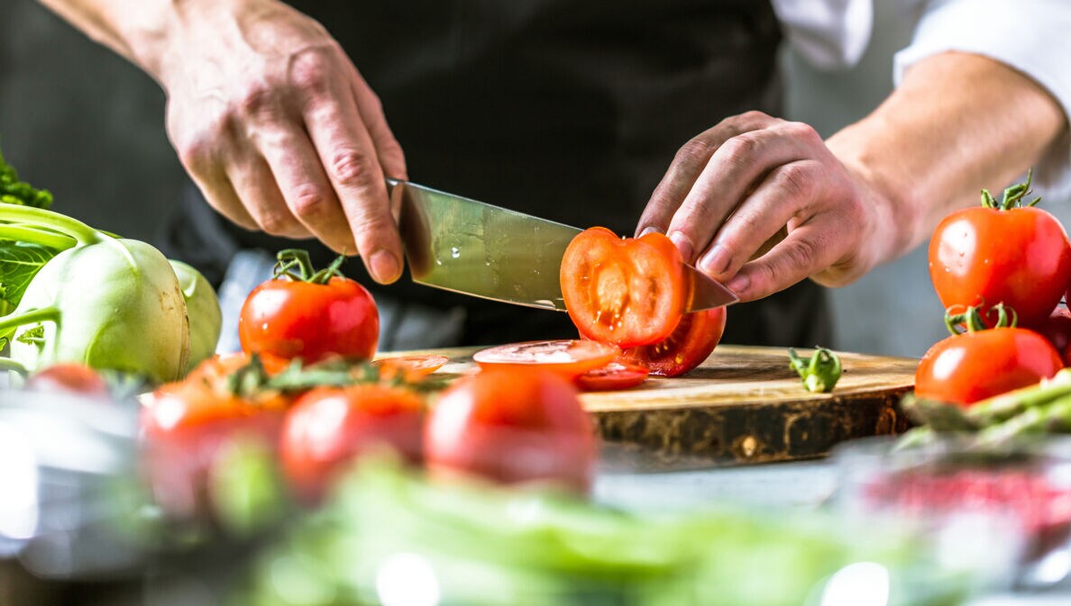 Hand mit Messer schneidet Tomaten
