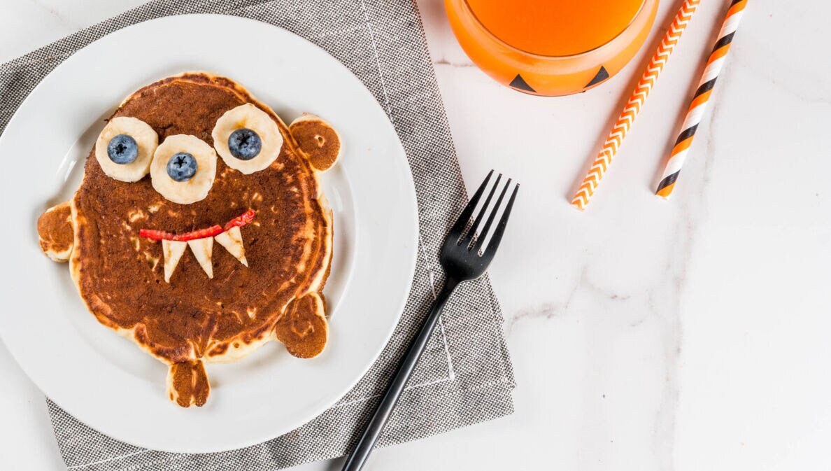 Frühstücksteller mit einem Pancake in Form eines kleinen Monsters, dessen Augen aus Bananen und Blaubeeren bestehen