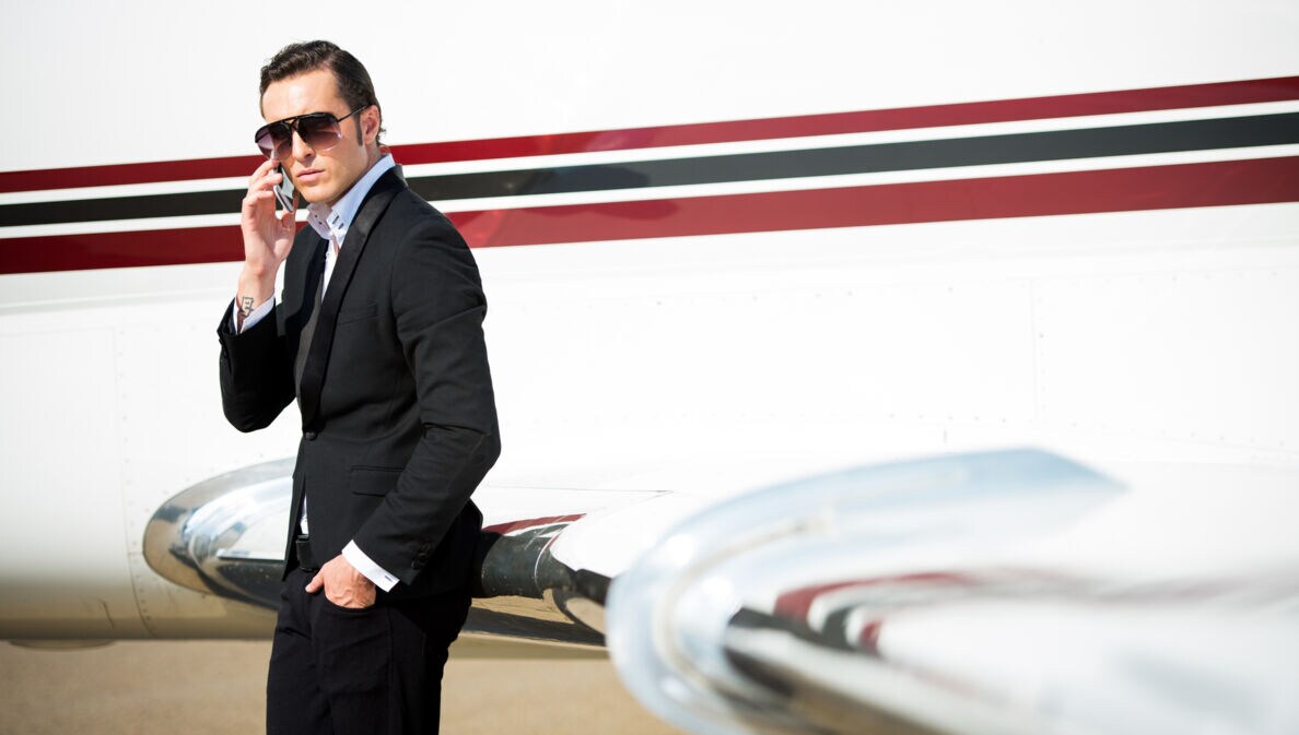 Junger Geschäftsmann neben dem Privatjet-Flugzeug, der mit seinem Smartphone telefoniert.