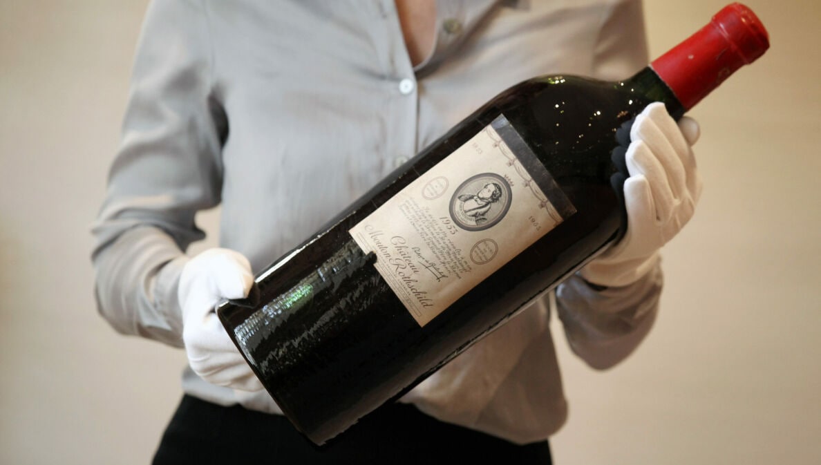 Eine große Flasche Rotwein der Marke Chateau Mouton Rothschild wir von einer Person mit weißen Handschuhen gehalten