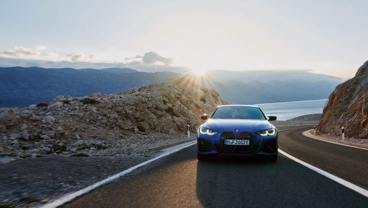 Vorderansicht eines blauen Autos der Marke BMW, das auf einer gebirgigen Küstenstraße fährt
