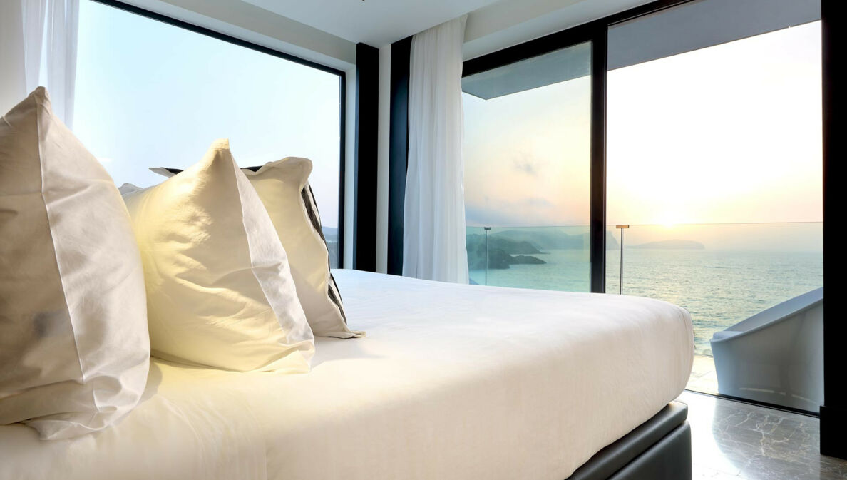Ein Bett in einem Hotelzimmer mit Blick auf das Meer und den Sonnenuntergang