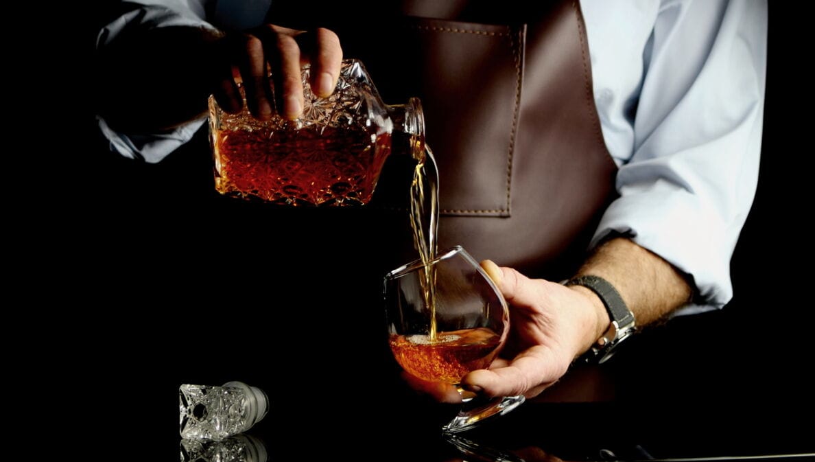 Ein Mann gießt Cognac aus einer Flasche ins Glas.