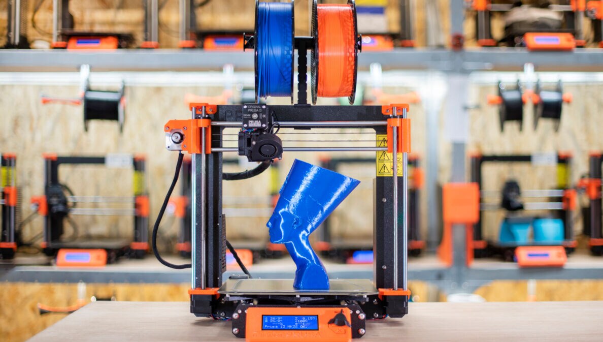 Ein 3D-Drucker mit Filament-Spulen und einer kleinen, gedruckten Nofretete-Büste aus blauem Kunststoff