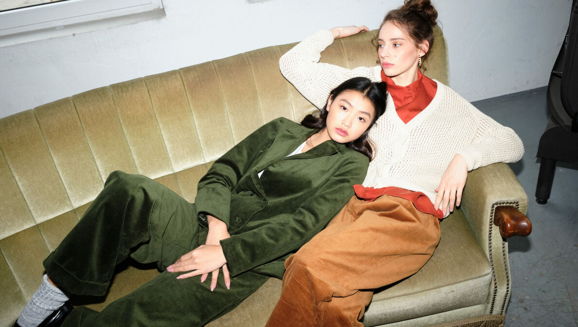 Zwei junge, stylish gekleidete Frauen in Cordhosen in herbstlichen Farben auf einem Sofa
