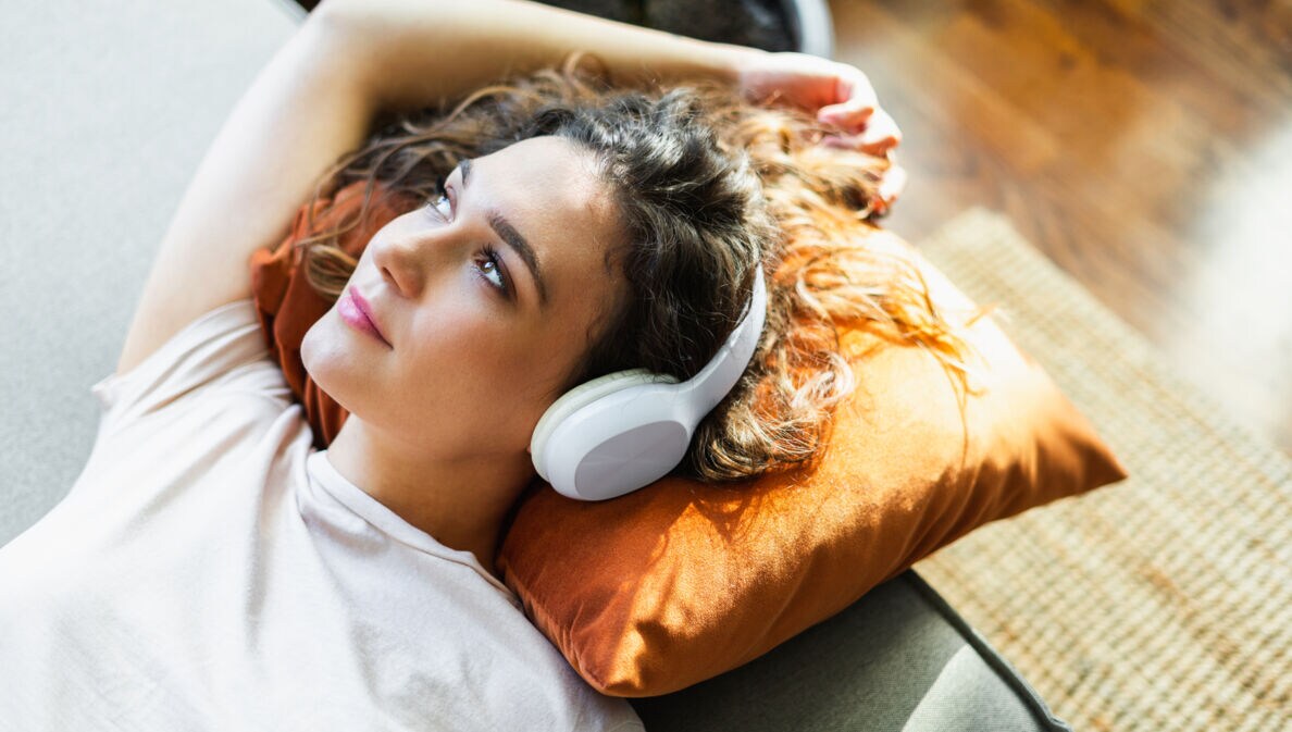 Eine Frau mit Kopfhörern liegt entspannt auf einem Sofa