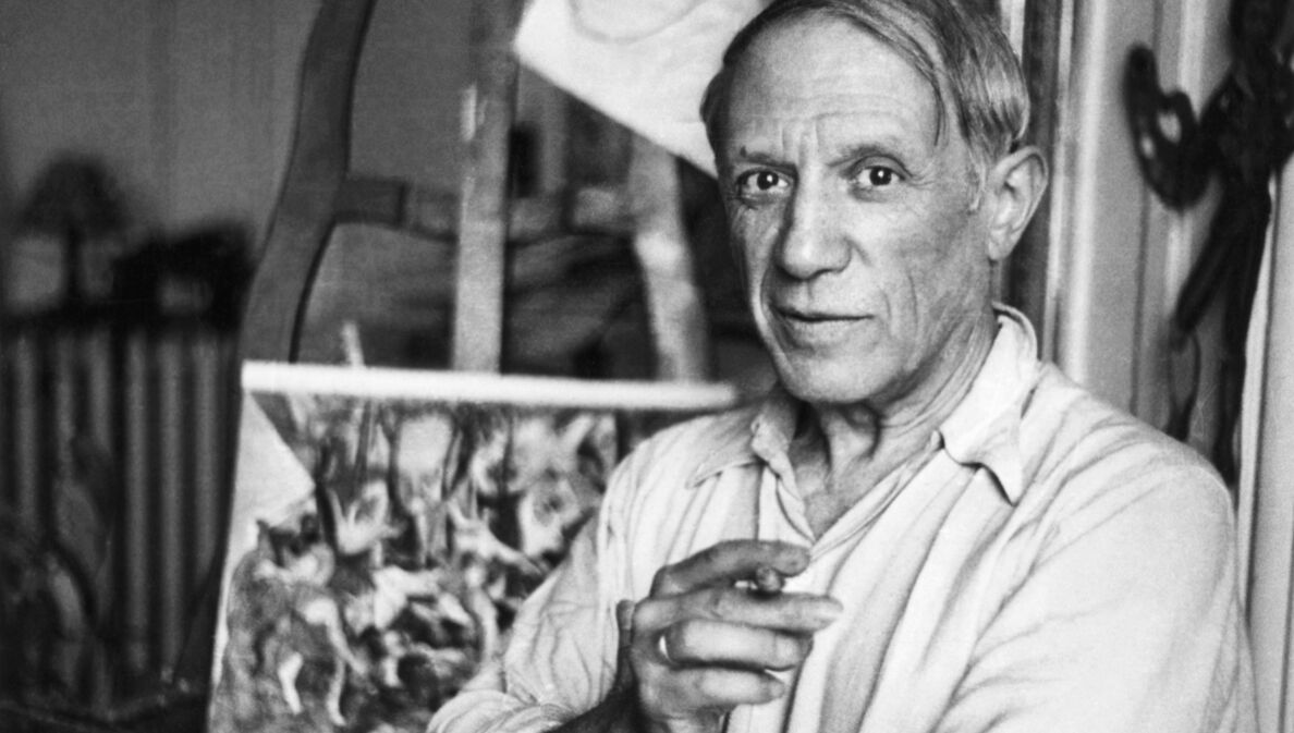 Schwarzweiß-Porträt von Pablo Picasso mit Zigarette in seinem Studio vor einer Staffelei, 1920