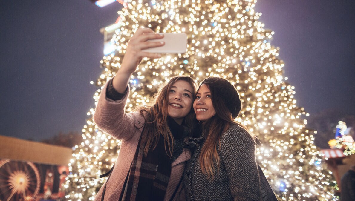Zwei Freundinnen machen ein Selfie vor einem erleuchteten Weihnachtsbaum