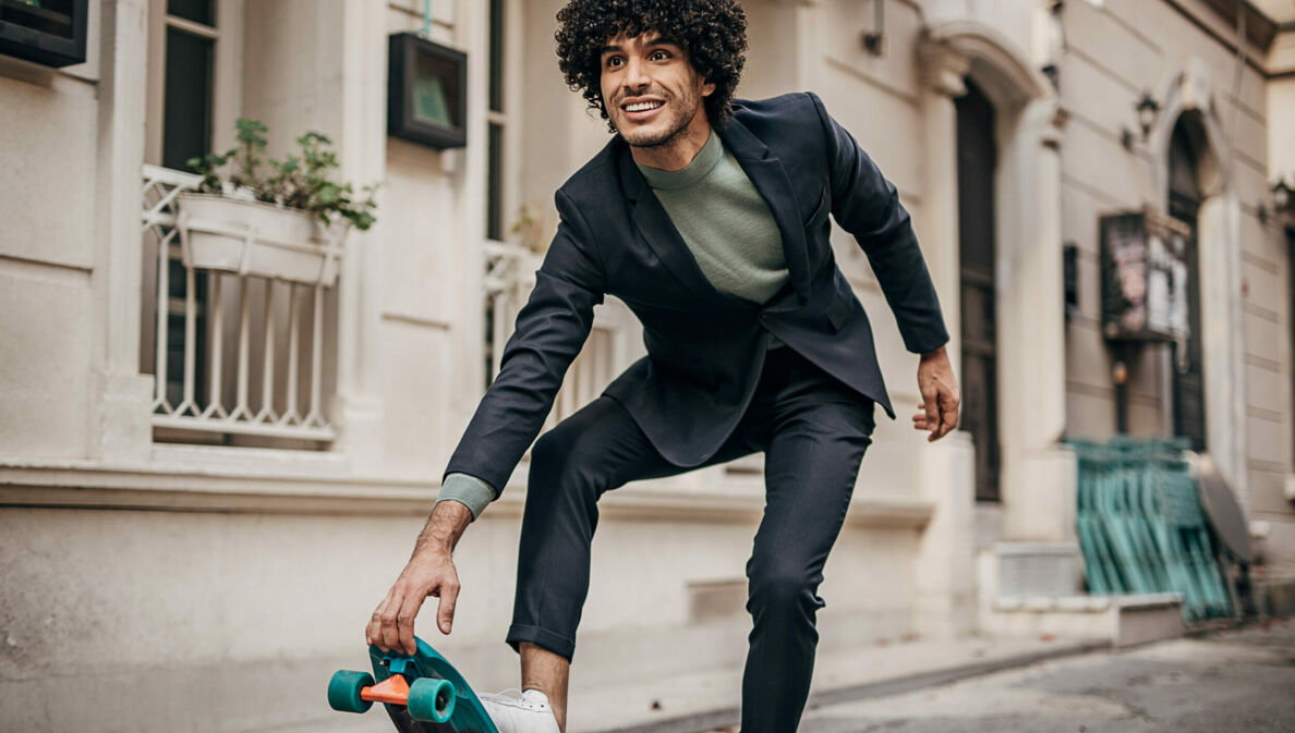 Ein junger Mann mit Anzug und Sneakern auf einem Skateboard in der Stadt